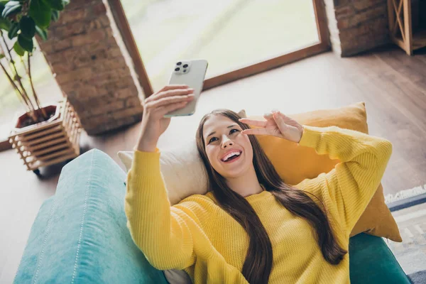 魅力的な興奮の女の子の敷設快適ソファホールドスマートフォン自画撮りデモンストレーションV Signリビングルームの家室内 — ストック写真
