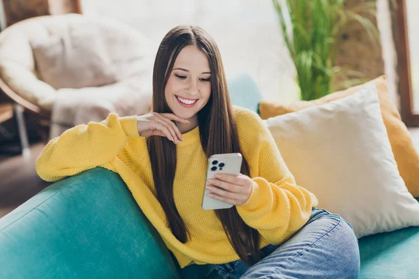 快乐漂亮的女孩坐在舒适的沙发上笑着用智能手机聊天室里的现代公寓 — 图库照片