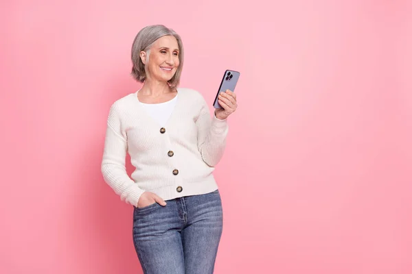 写真のシニア女性ホールドデバイス使用Instagramの電報Twitter Facebook着用トレンディーな白い服ピンク色の背景に孤立 — ストック写真