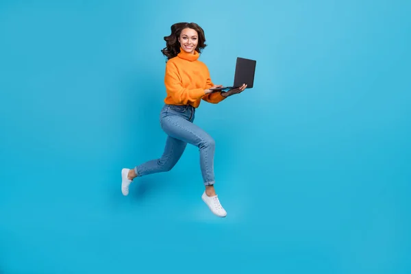 全长照片甜美快乐的女人穿着橙色毛衣跳着工作的现代装置孤立的蓝色背景 — 图库照片