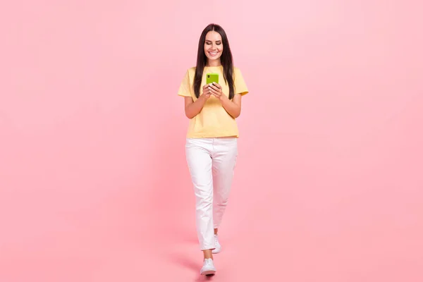 フル長さ写真の光沢のあるかわいい女性の服黄色Tシャツ歩行チャットIphone現代デバイス孤立ピンク色の背景 — ストック写真