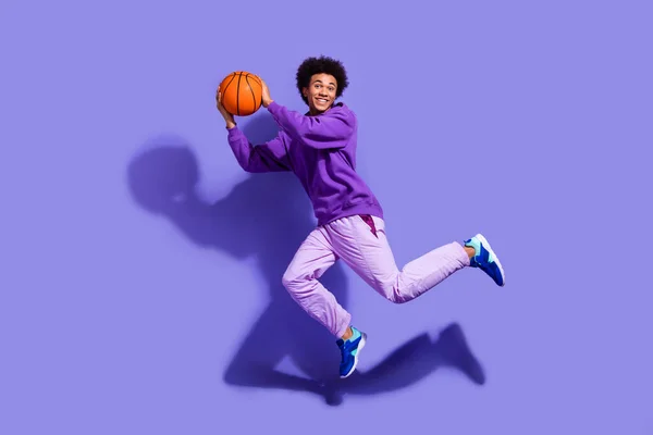 全长照片上 精力充沛的小伙子身穿紫罗兰色运动服 把篮子扔到紫色背景的篮子里 — 图库照片