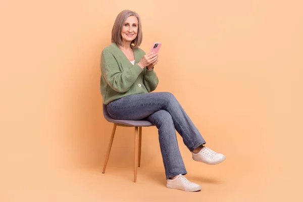 完全な長さ体の座ってリラックスした椅子祖母を探索新しい技術を使用して電話ブラウジングGoogle隔離上ベージュ色の背景 — ストック写真