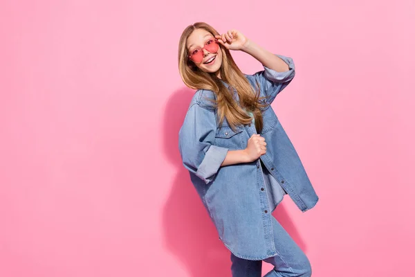 若い十代の女の子の写真のポートレートはピンクの色の背景に隔離された流行のジーンズの衣装を身に着けているタッチサングラスショッピングプロモーション — ストック写真