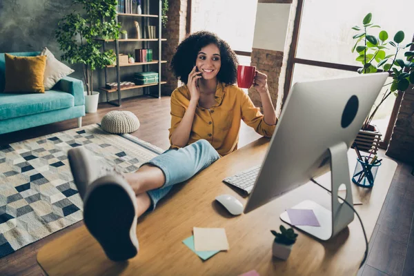 全尺寸照片迷人的企业代理女孩把腿放在桌面上讲电话手持茶杯工作站在室内 — 图库照片