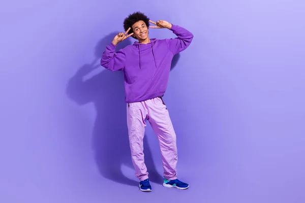 stock image Full length photo of funky carefree guy wear purple sportswear pullover showing v-sign on head isolated on violet color background.