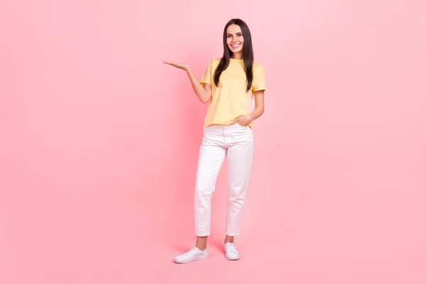 フル長さ写真のかなりかわいい女性身に着けている黄色Tシャツ保持アーム空のスペース孤立ピンク色の背景 — ストック写真