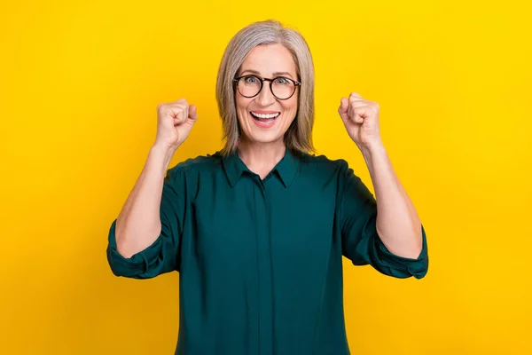 Photo of ecstatic agent aged lady raising fists up achieving business goals isolated bright color background.