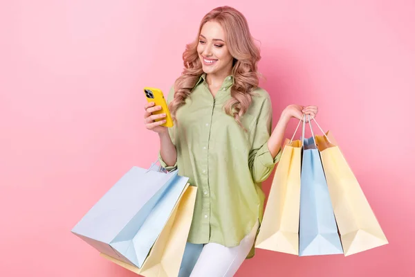 かわいい女性の写真は 現代的なデバイスを保持パッケージを保持見て緑のシャツを身に着けている孤立ピンク色の背景 — ストック写真