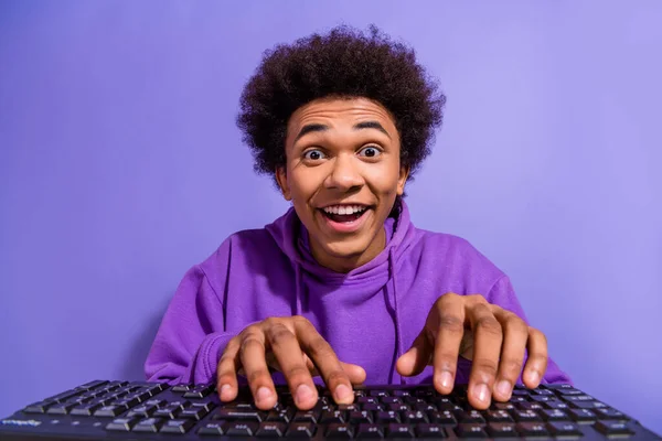 照片上 一个喜形于色的家伙穿着紫色套头衫 在电脑键盘上聊天 背景为紫罗兰色 — 图库照片