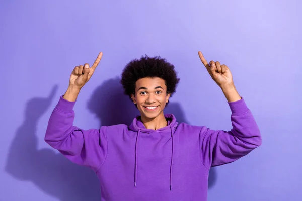 Portrait of positive person toothy smile direct fingers up above empty space offer isolated on purple color background.