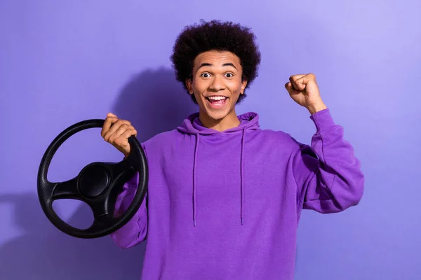 Photo of ecstatic overjoyed guy afro hairdo dressed purple pullover hold steering wheel win new car isolated on violet color background.