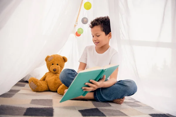 聪明学童读书讲故事的照片泰迪熊在家里舒适的帐篷里 在幼儿园的游戏室里 — 图库照片