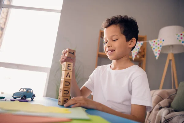 魅力的なかなり小さな男の子の写真白いTシャツを着てテーブルに座って学習文字を学びますタワー屋内部屋の家を作る — ストック写真