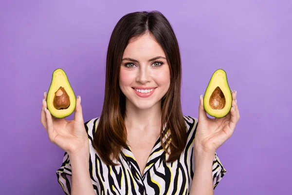 Portrait of cheerful nice girl beaming smile arms hold two halves avocado isolated on purple color background.