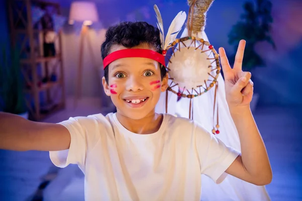 stock image Photo of positive funny cute boy playing game native indians with friends on internet connection make selfie v sign in evening playroom.