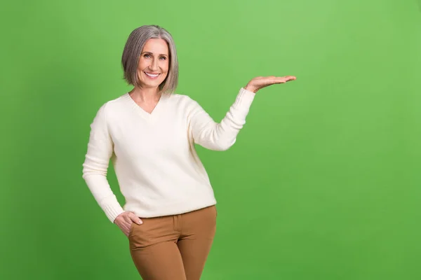 正直な笑顔の祖母の種類の写真は 白いプルオーバーを着用腕のプレゼンテーションを保持する新しい安価な製品の提供は 緑の色の背景に隔離 — ストック写真