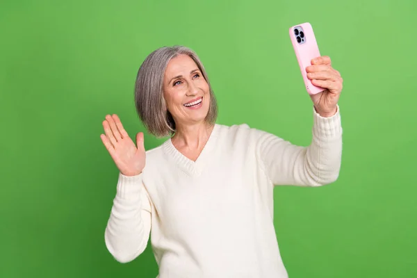照片上的高年级滑稽女子波布灰白头发身穿白色套头衫挥臂打招呼电话视频隔离在绿色背景下 — 图库照片