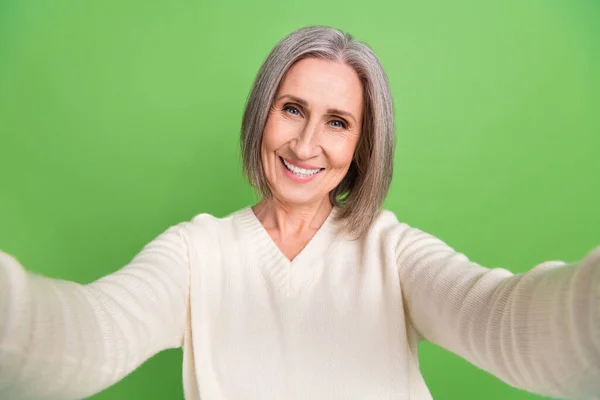 セルフィービデオの年金受給者の女性灰色の髪の祖母の記録ビデオ持っています楽しい摩耗白いシャツ新しいビデオ隔離された緑の色の背景 — ストック写真