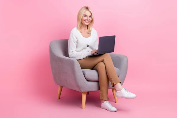 明るいの完全な長さの肖像画かなり女性座って快適な椅子使用ワイヤレスネットブック隔離されたピンク色の背景 — ストック写真