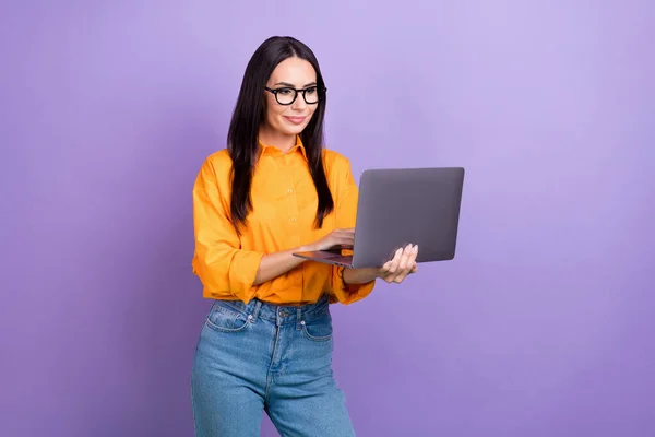 若い自信起業家の女性の写真オレンジのシャツを着てノートパソコンのズームミーティング作業の瞬間を保持紫色の背景に隔離された — ストック写真