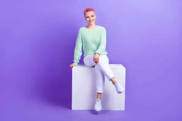 完全な長さ写真の可愛いです女性の服を着たティールプルオーバー座って白いプラットフォーム隔離された紫色の背景 — ストック写真