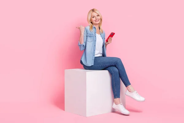 フルボディ写真の中年ビジネス女性コンテンツメーカーSmm Targelogist座ってプラットフォーム直接指Mokup隔離されたピンクの背景 — ストック写真