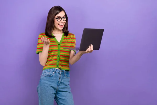 快乐愉快的女人的照片直发式穿着五颜六色的T恤衫看着笔记本电脑 通过视频通话隔离在紫色背景下 — 图库照片