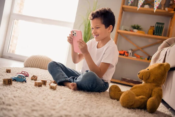 Foto Von Positiven Jungen Sitzen Bodenteppich Vorschulinterieur Verwenden Gadget Wählen — Stockfoto