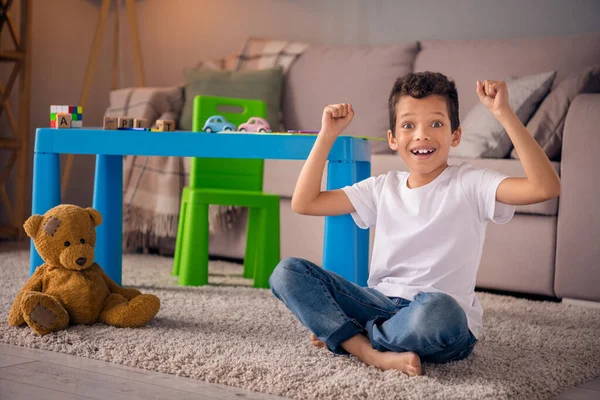 兴奋的小男孩坐在地板上舒服舒适的游戏室举起拳头等着最好的父母 — 图库照片