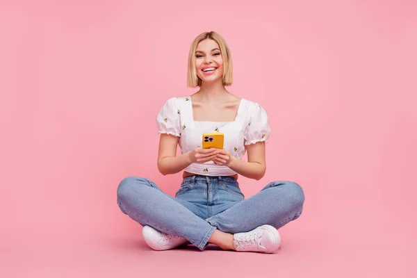若い素敵な女性のブログの完全なボディ幹部はピンクの色の背景に隔離されたオンラインスマートフォンに座ってチャットを書く — ストック写真