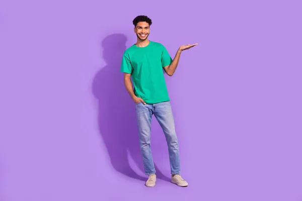 全长照片中的年轻人穿着时髦的T恤衫手握着他的品牌产品学生折扣造型与紫色背景隔离 — 图库照片