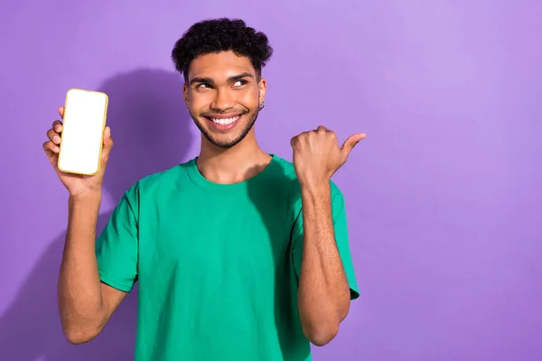 照片上的年轻人穿着绿色T恤衫 手指空空如也 手持电话 推荐在线服务 隔离紫色背景 — 图库照片
