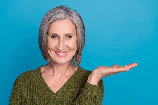漂亮的退休女士笑着微笑的合影拿着敞开大门的棕榈广告穿着卡其色毛衣孤立的蓝色背景 — 图库照片