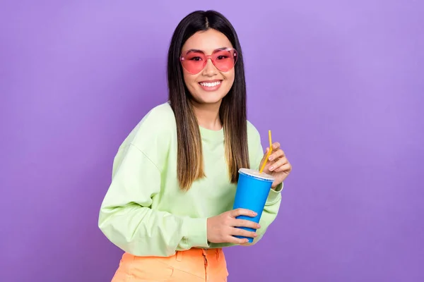 Photo of cheerful girlish good mood woman with dyed hairdo dressed green pullover hold soda cup isolated on purple color background.