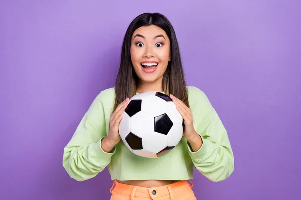 令人印象深刻的积极向上的女孩 身穿时髦的套头衫 手挽着足球 凝视着紫色背景的足球 — 图库照片