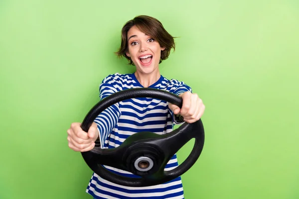 年轻兴奋的泡泡头发女人拿着方向盘高速疯狂驾驶购买绿色背景的新型电动汽车的照片 — 图库照片