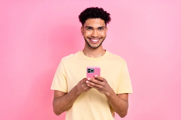 照片上的帅哥与非洲发型穿着黄色T恤阅读通知智能手机孤立的粉红色背景 — 图库照片