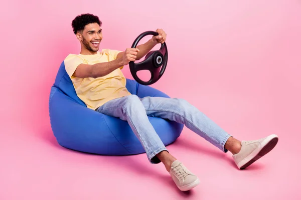 若いクレイジー男運転のフルボディ写真彼の賃貸自動車シミュレータアプリを保持ステアリングホイール座ってPoufピンク色の背景に孤立 — ストック写真