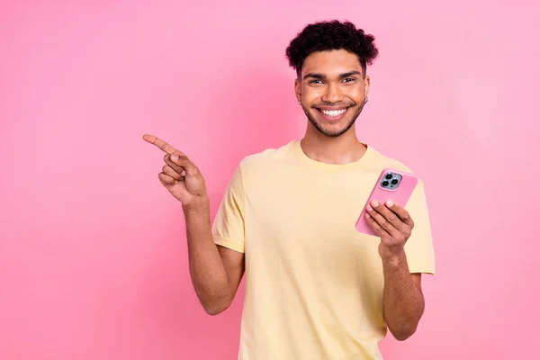 stock image Photo of funny guy afro coiffure dressed yellow t-shirt hold smartphone indicating at eshop empty space isolated on pink color background.