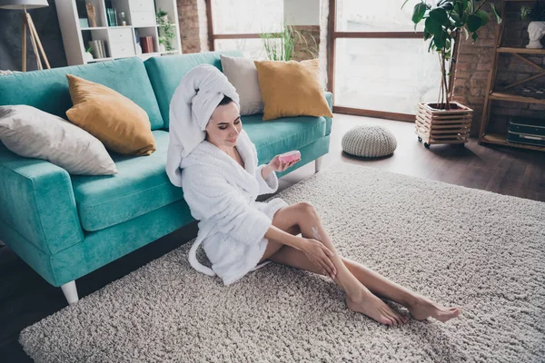 Stock image Photo of young stunning woman after legs shaving spa salon procedure sitting floor near cozy divan apply cream legs skin indoors.