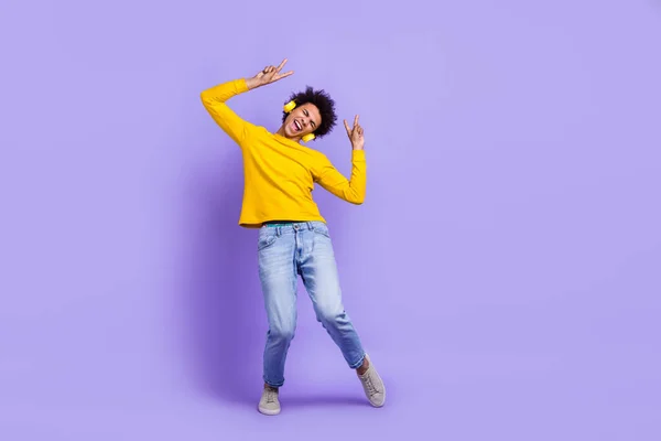 Full size photo of cool guy dressed yellow long sleeve headphones dancing having fun show v-sign isolated on purple color background.