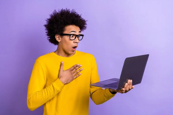 年轻人惊讶的手胸前的照片震惊了阅读关于紫色背景下孤立的通货膨胀的坏消息的笔记本电脑 — 图库照片