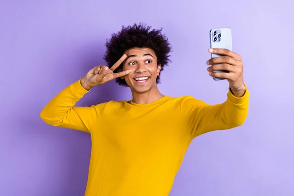 Portrait of funky excited person hold smart phone take selfie show v-sign near eye isolated on purple color background.