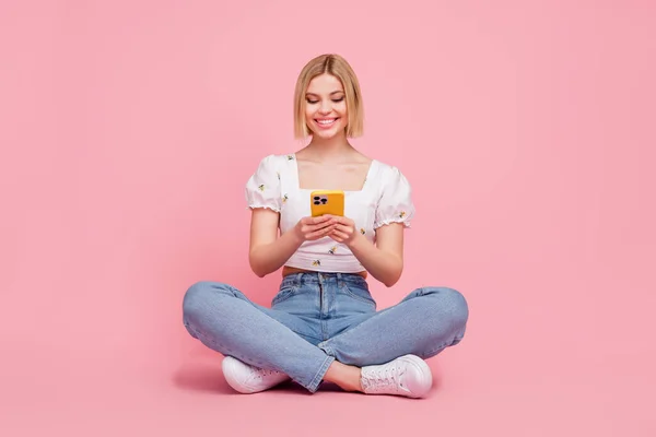 フルボディサイズ写真の若いです女性座っていますとともに彼女のお気に入りの現代的なガジェットスマートフォンのテキストメッセージMsチャット孤立したピンク色の背景 — ストック写真