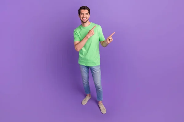 フル長さサイズ写真の若い男身に着けている緑スタイリッシュなTシャツジーンズ直接指空のスペース広告隔離された上に紫色の色背景 — ストック写真
