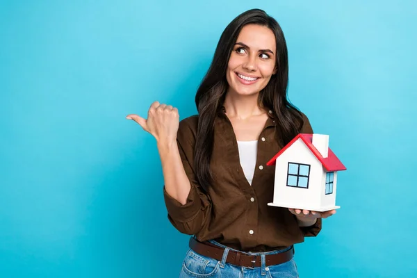 照片上 一位心事重重的女士穿着棕色的衬衫 手里拿着一幢小房子 看上去像大拇指空空如也 只有蓝色的背景 — 图库照片
