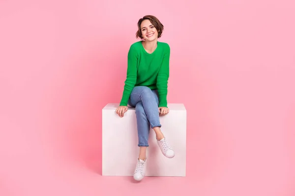 フル長いです写真のファンキー可愛いです女の子身に着けている緑のセーター笑顔座ってプラットフォーム隔離されたピンク色の背景 — ストック写真