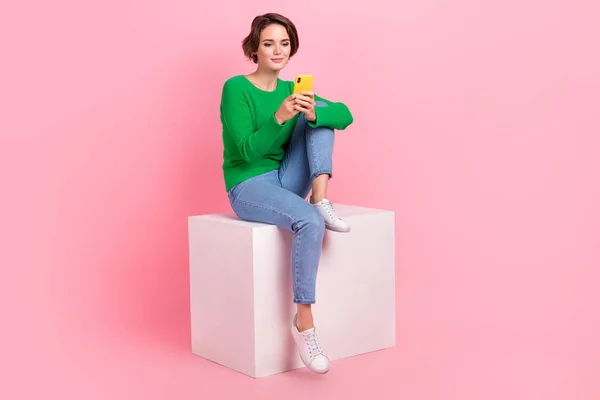 可愛い女の子の完全な長さの写真はスタイリッシュな服を着て座るキューブはピンクの色の背景に隔離された現代的な技術サムスンのIphoneを使用 — ストック写真
