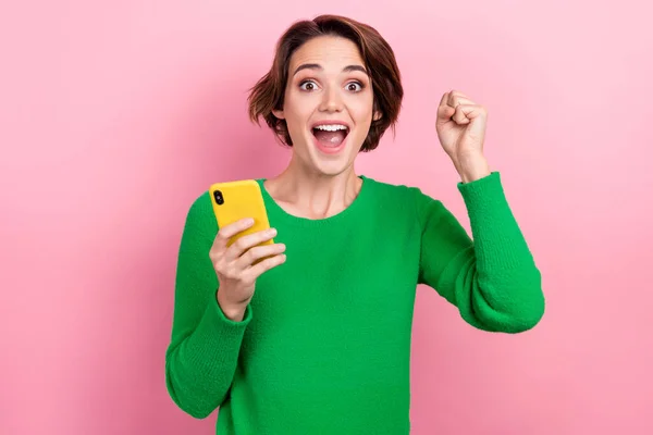 かわいいですラッキー女の子の服を着た緑のセーター立ち上がり拳通信現代デバイス隔離されたピンク色の背景 — ストック写真